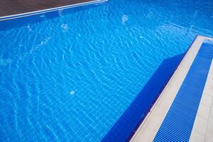 Crystal clear swimming pool under bright sunlight with reflections creating a serene atmosphere photo