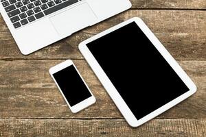 Modern workspace with laptop, tablet, and smartphone on rustic wooden desk during daytime photo