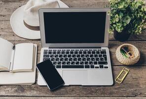 Workspace setup with a laptop, smartphone, notebook, and plant on a wooden table during daylight photo