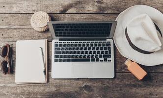 Relaxed workspace setup with a laptop, notebook, and summer accessories on a wooden table photo