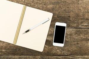 Workspace setup with a blank notebook, pen, and smartphone on a rustic wooden table photo