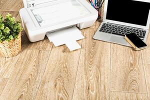 Working from home with a printer, laptop, and mobile phone on a wooden floor, suitable for productivity and organization photo