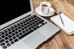 Workspace setup with laptop coffee and notepad on wooden table during early morning hours photo