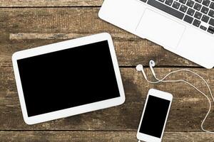 Workspace setup featuring tablet, smartphone, and laptop on rustic wooden table during daytime photo