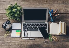Workspace featuring a laptop, notepad, and office supplies on a rustic wooden table in a well-lit environment photo