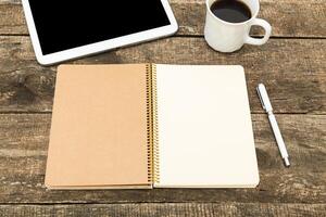Blank notebook and tablet on a wooden table with a cup of coffee ready for writing or brainstorming ideas in a cozy workspace photo