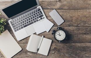 Workspace setup with laptop, clock, and notepad on wooden table during morning hours photo