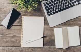 Workspace with a laptop, smartphone, and notepads on a wooden table ready for productive tasks photo