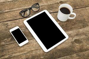 Digital devices and a coffee cup arranged neatly on a rustic wooden desk during a cozy working session photo