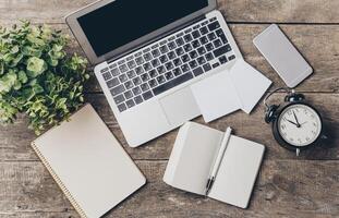 Workstation setup with laptop, clock, and notepads on wooden desk in a cozy and organized environment photo