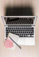 Workspace setup featuring a laptop, notepad, and stationery on a wooden table during daytime photo
