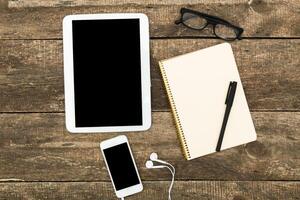 Digital workspace setup with tablet, smartphone, notebook, pen, and glasses on wooden table photo