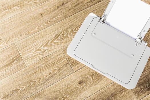Printer placed on a wooden floor surrounded by a clean workspace with empty paper tray, indicating readiness for printing tasks photo