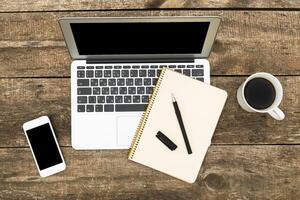 Workspace setup with a laptop, notebook, pen, smartphone, and coffee on a rustic wooden table photo