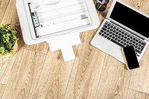 Working environment with a laptop, printer, and smartphone on a wooden desk during the day photo