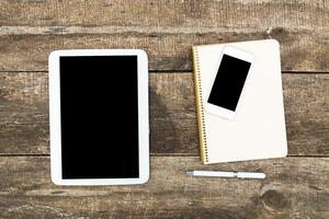 Workspace setup with tablet, smartphone, notebook, and pen on a rustic wooden table conducive for productivity photo