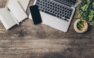 Workspace setup with laptop, smartphone, notebook, and plants on rustic wooden table in a cozy environment photo