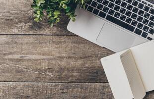 Workspace setup with a laptop, notebook, and plant on rustic wooden table during the day photo
