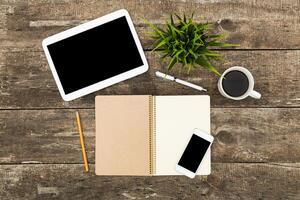 Workspace setup with digital devices, stationery, and a coffee cup on a rustic wooden table photo