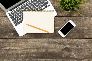 Workspace setup with laptop, smartphone, notepad, and pencil on wooden table during daytime photo