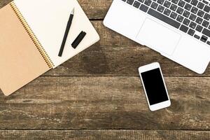 Notepad, pen, smartphone, and laptop arranged on wooden table for creative brainstorming session photo