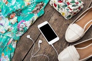 Bright floral dress and accessories arranged on wooden surface with smartphone and earphones displayed in a relaxing afternoon setup photo