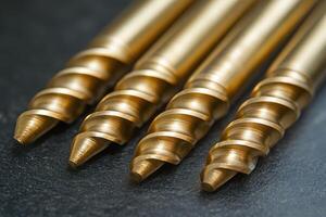 Golden drill bits resting on dark surface showing sharp threads photo
