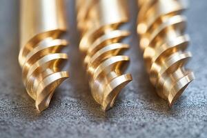 Golden drill bits resting on dark surface showing sharp threads. photo