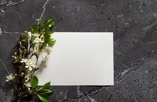 The photograph captures a carefully arranged scene with a blank card, ribbon, and flowers, creating a visual invitation to a personal message or event photo