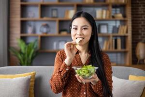 Asian woman in relaxed setting enjoying fresh salad, emphasizing healthy eating and positive lifestyle. Her expression shows satisfaction and commitment to wellness and nutrition. photo