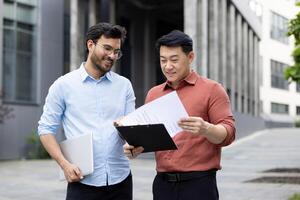 Two colleagues of office company employees discussing financial reports, contracts and documents, group of business people outside office building with papers in hands discussing. photo