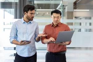 Two office workers serious and concentrated discussing work project while standing inside office at workplace. Men looking at laptop screen, online reporting and data. photo