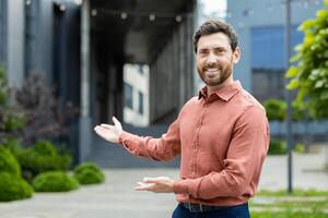 Successful man invites to work in a new team. Businessman looks at the camera and holds hands to the side in a gesture of greeting and invitation. photo