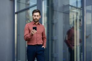 Confident businessman using smartphone outdoors in urban setting, reflecting professionalism and communication. Man wearing casual smart attire, focused on task. Keywords. businessman, smartphone. photo