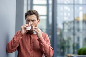 Man using tissue outdoors in urban setting, wearing casual shirt, looking concerned. Scene depicts health issues like cold or allergies, reflecting everyday challenges in wellness and hygiene. photo