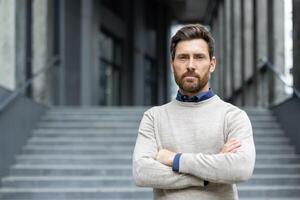 Confident businessman with beard stands with arms crossed, exuding strength and determination. Professional attire emphasizes leadership qualities. photo