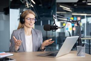 Mature woman businesswoman in a modern office setting, using headphones and a microphone for podcast production. The image portrays professionalism and highlights a technological workspace. photo
