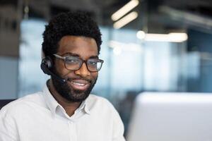 Portrait of a support worker, a man with a headset smiling and looking at the camera. A company employee close-up with a laptop inside the office photo