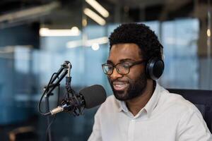Blogger influencer close up, man with headphones using professional microphone to record podcast. African American working in studio in evening, narrating and recording training course. photo