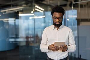 Serious thinking businessman with tablet computer in hands. Young man in business clothes using app, reading email and viewing financial data online. photo