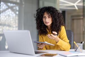 Successful woman with notebook in hands watching course, online business meeting conference. Office worker uses laptop for call, communicates with colleagues remotely. photo