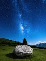 Milky way over a boulder in a grassy field at night photo