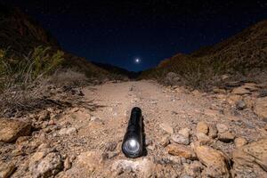 A flashlight illuminates a rocky desert path under a starry night sky photo
