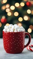 steaming mug of hot cocoa with marshmallows a candy cane and a Christmas tree glowing softly in the blurry background photo