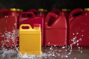 Front view of yellow plastic motor oil bottle splashed by stream of water, container with handle and red screw cap without label photo