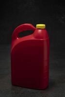Three-quarter view of red plastic motor oil bottle with handle and yellow screw-top without label on dark ceramic photo