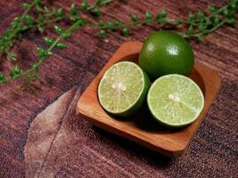 Closeup Fresh limes, consisting of one whole lime and two slices, neatly arranged on a small wooden plate. With brown background and decorative leaves enhance the natural. photo