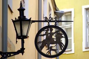 A close-up of a vintage street lamp with an ornate design and decorative sign. Traditional European street with colorful buildings in the background. Concept of old-world charm and historical detail photo
