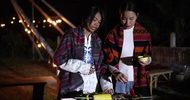 Handheld shot, Two Asian women dressed in warm clothing talk and share a happy moment together while grilling food and enjoying the cold night. video