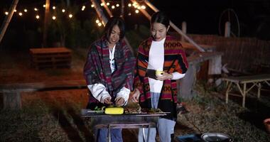 Handheld high angle view shot,Two Asian women dressed in warm clothing talk and share a happy moment together while grilling food video